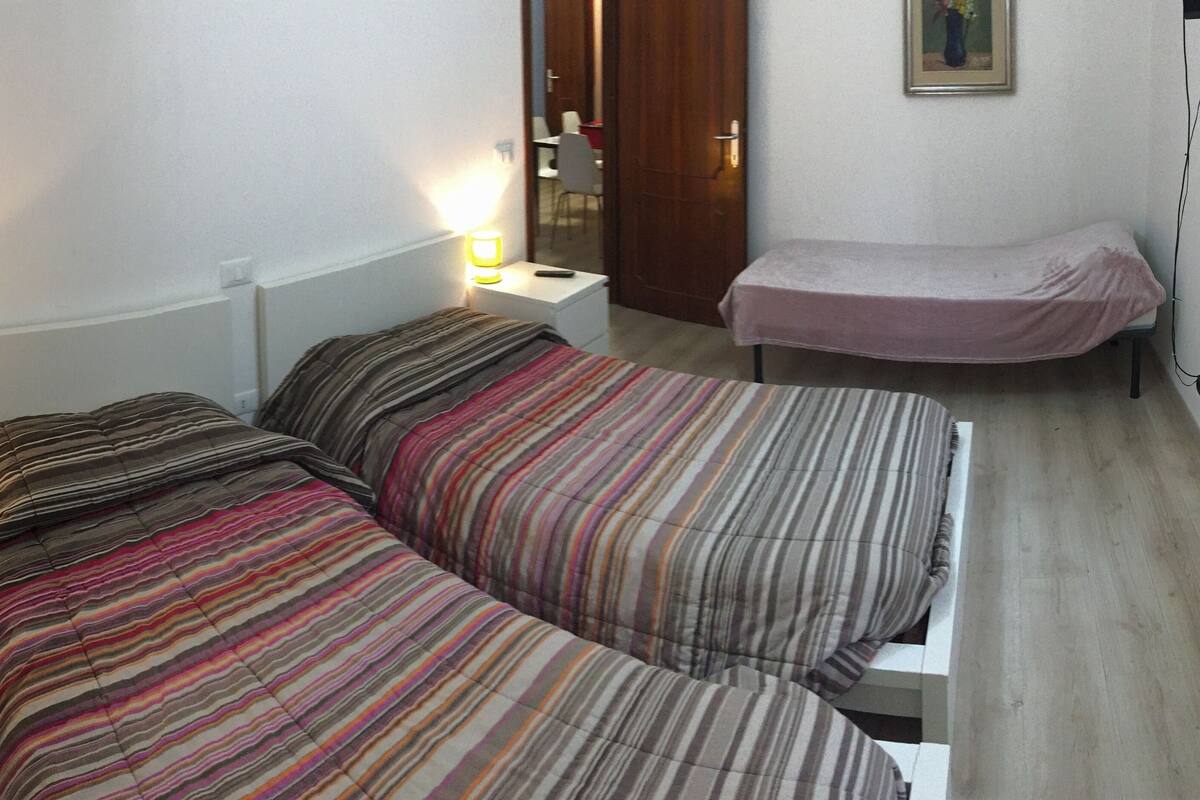 A room with two beds, a nightstand with a lamp, a small table, and a radiator.