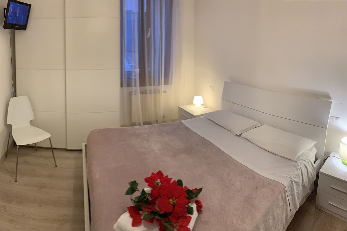 A hotel room with a bed, a chair, a bedside table with a lamp, and a television on the wall.