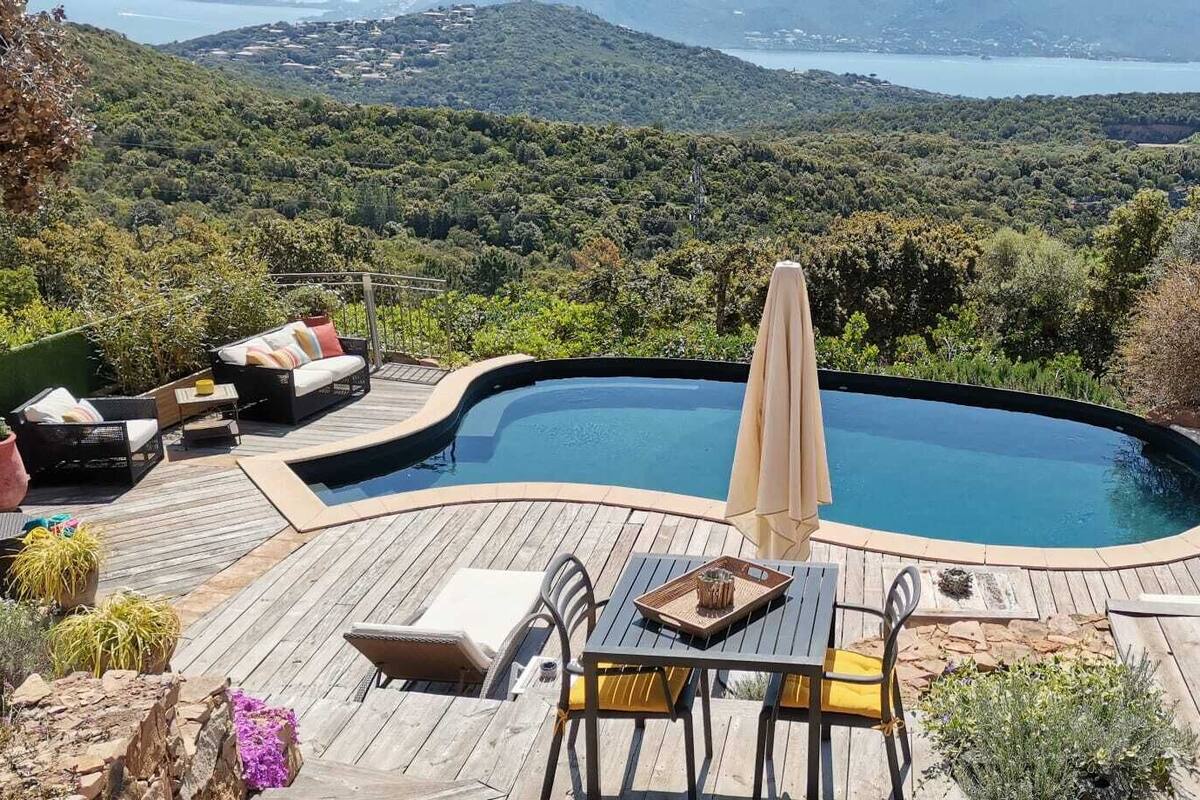 Une piscine avec un jacuzzi, entourée d’une terrasse en bois, de mobilier d’extérieur et offrant une vue panoramique sur des collines et un lac.