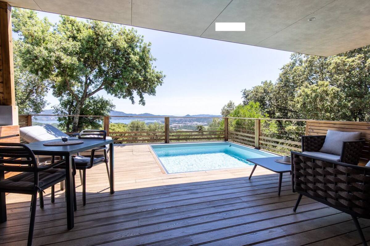 Une terrasse avec une piscine, des meubles en bois et une vue sur la mer et les collines.