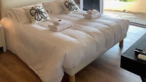 Un dormitorio con una cama grande, una mesita de noche, una lámpara y vistas al exterior a través de una puerta corredera.