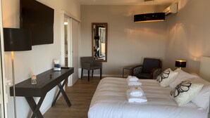 Habitación de hotel con cama, escritorio, silla, televisor y aire acondicionado.