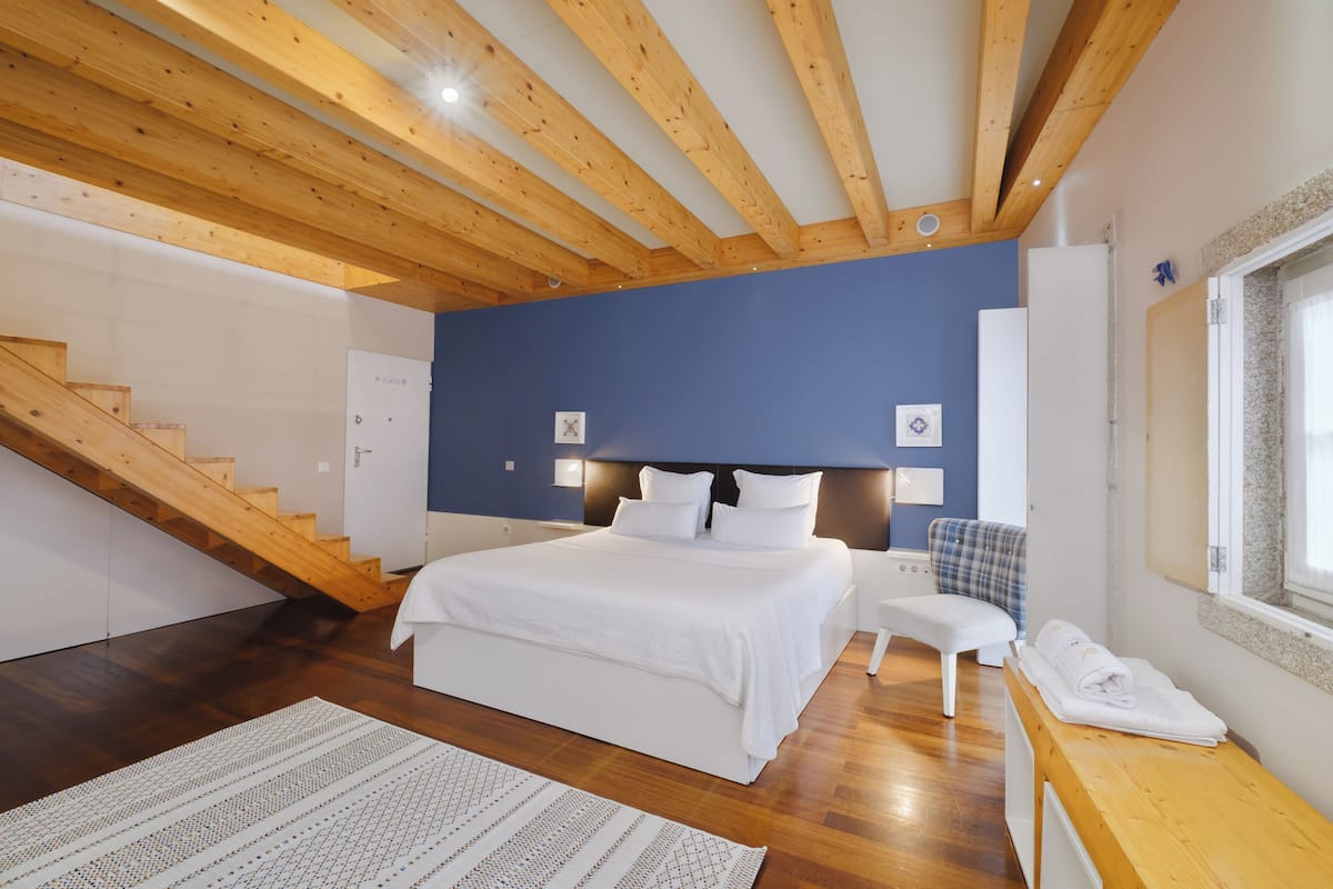 A bedroom with a wooden ceiling, a bed, a chair, a desk, and a window.