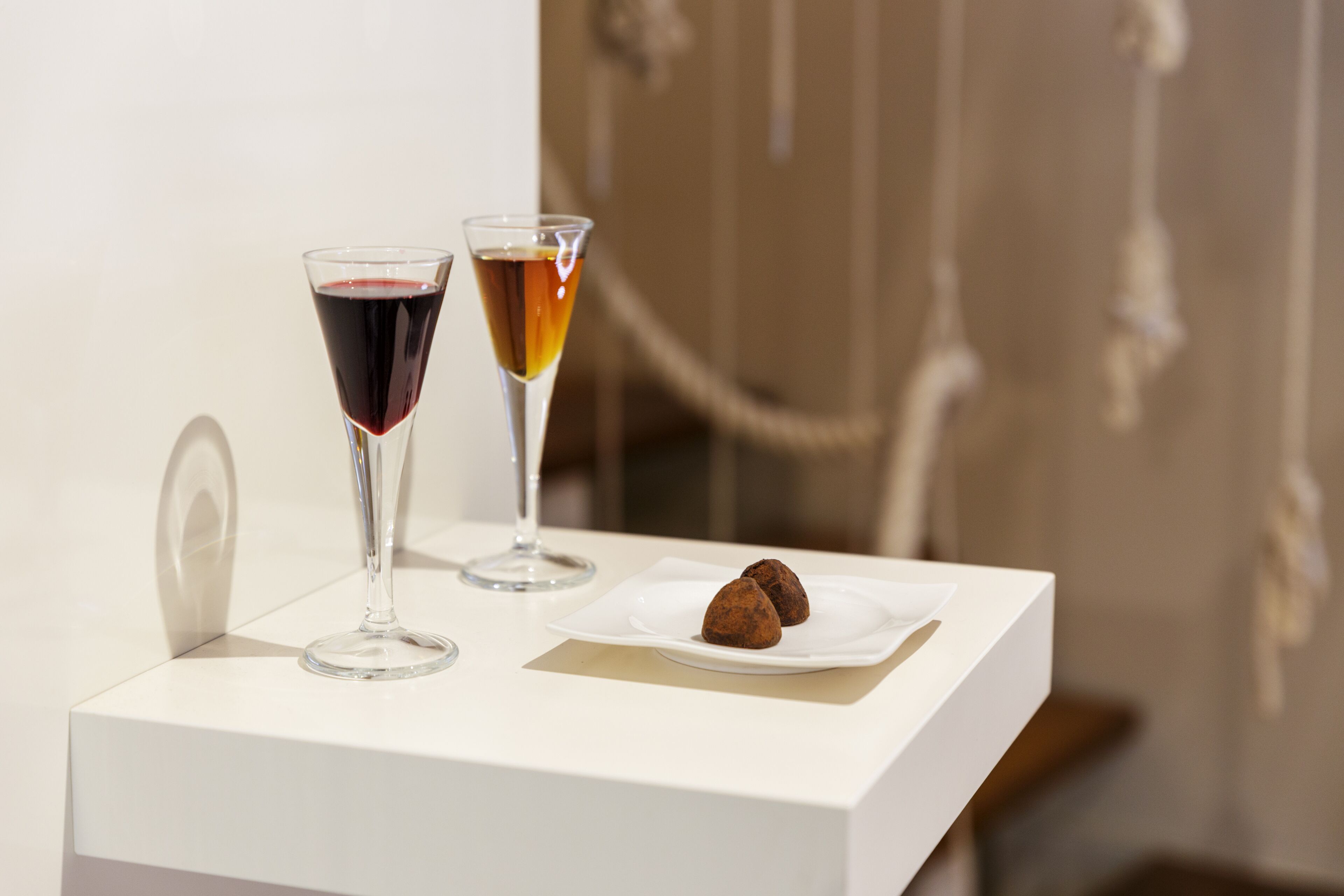 A white table with two glasses of wine and a plate with two chocolate truffles.