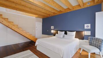 A bedroom with a wooden staircase, a bed with white bedding, a nightstand, and a chair.