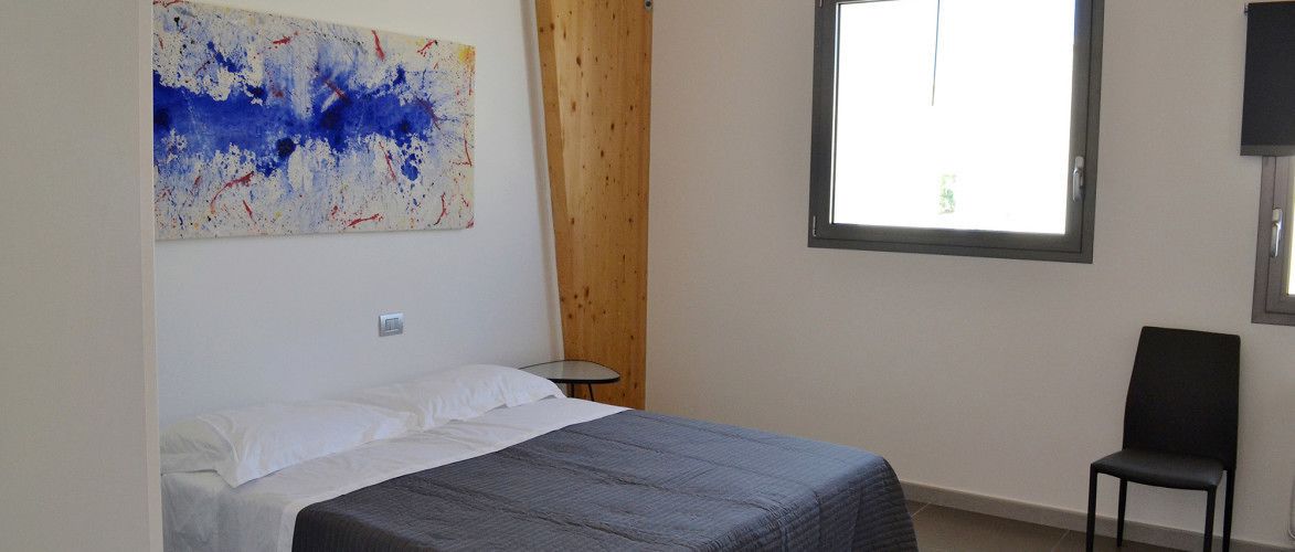 A bedroom with a bed, a chair, a small table, a window, and a painting on the wall.