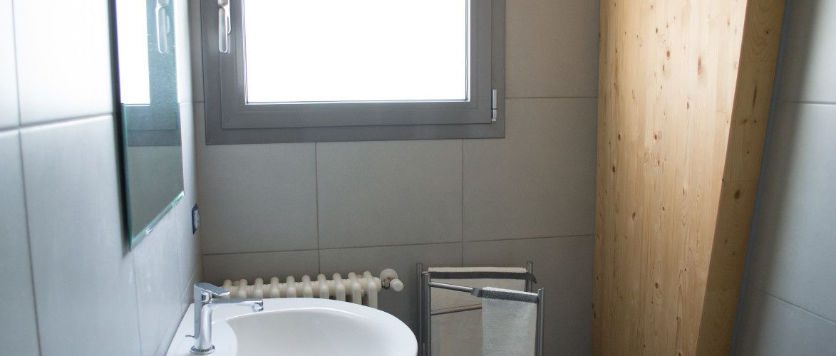 A bathroom with a white sink, a mirror, a window, and a towel rack.