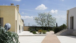 Ein Innenhof mit einem Weg, der zu einem Gebäude führt, umgeben von Grünflächen und blauem Himmel.