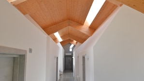 Ein Korridor mit Holzbalkendecke, weißen Wänden und Fliesenboden.