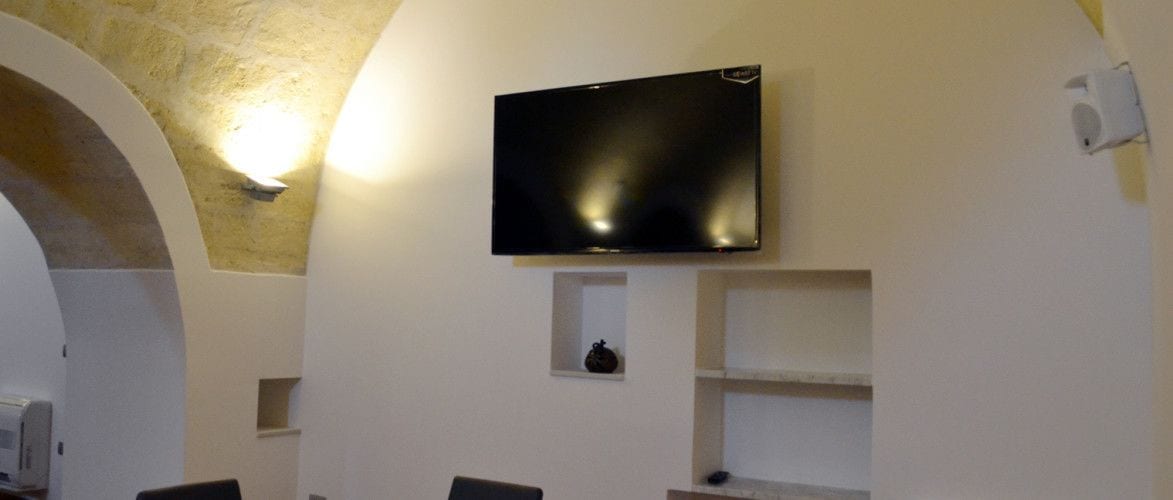 Una stanza con una TV a schermo piatto fissata al muro, un piccolo ripiano con un oggetto decorativo e un arco in pietra.