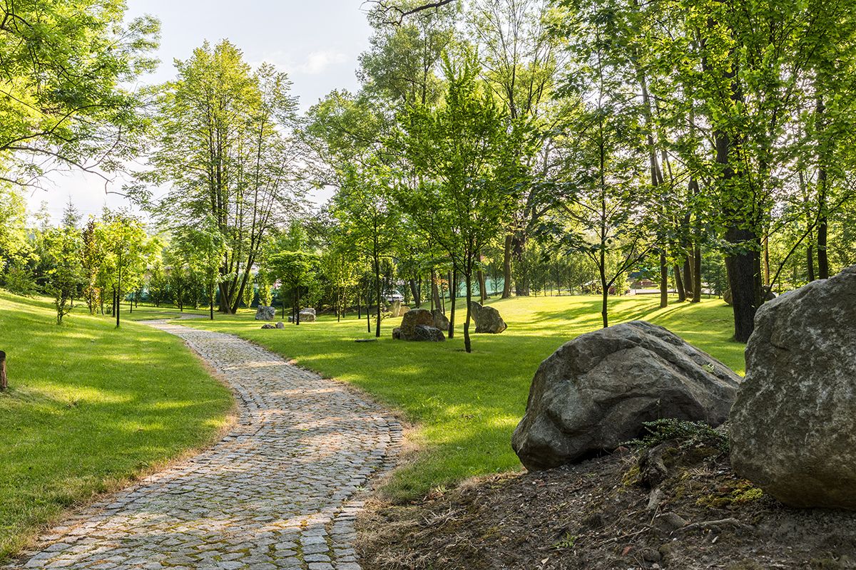 Un sentiero acciottolato serpeggia attraverso un parco, punteggiato da grandi rocce e alberi.