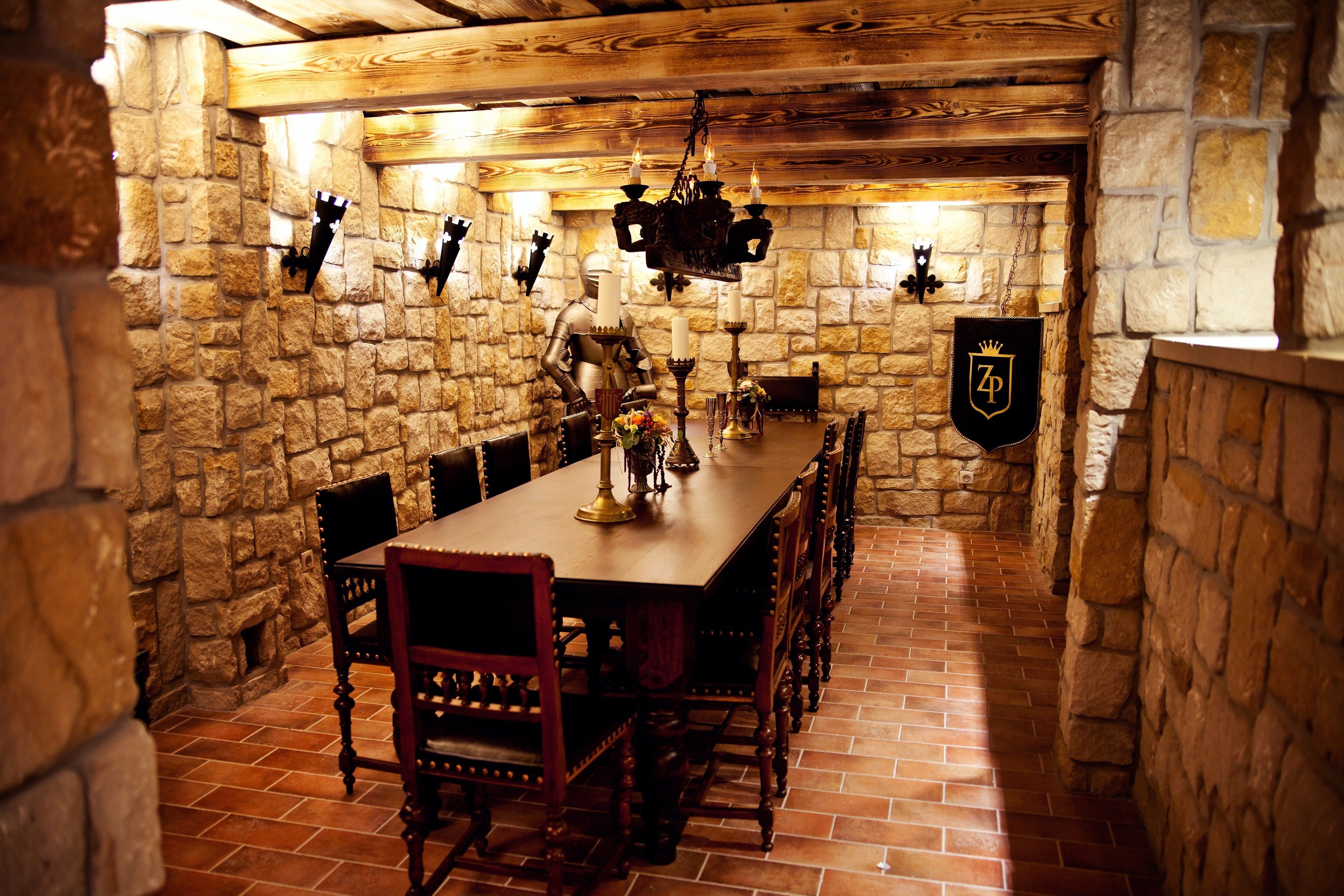 A stone-walled dining room with a long wooden table, chairs, and a chandelier.