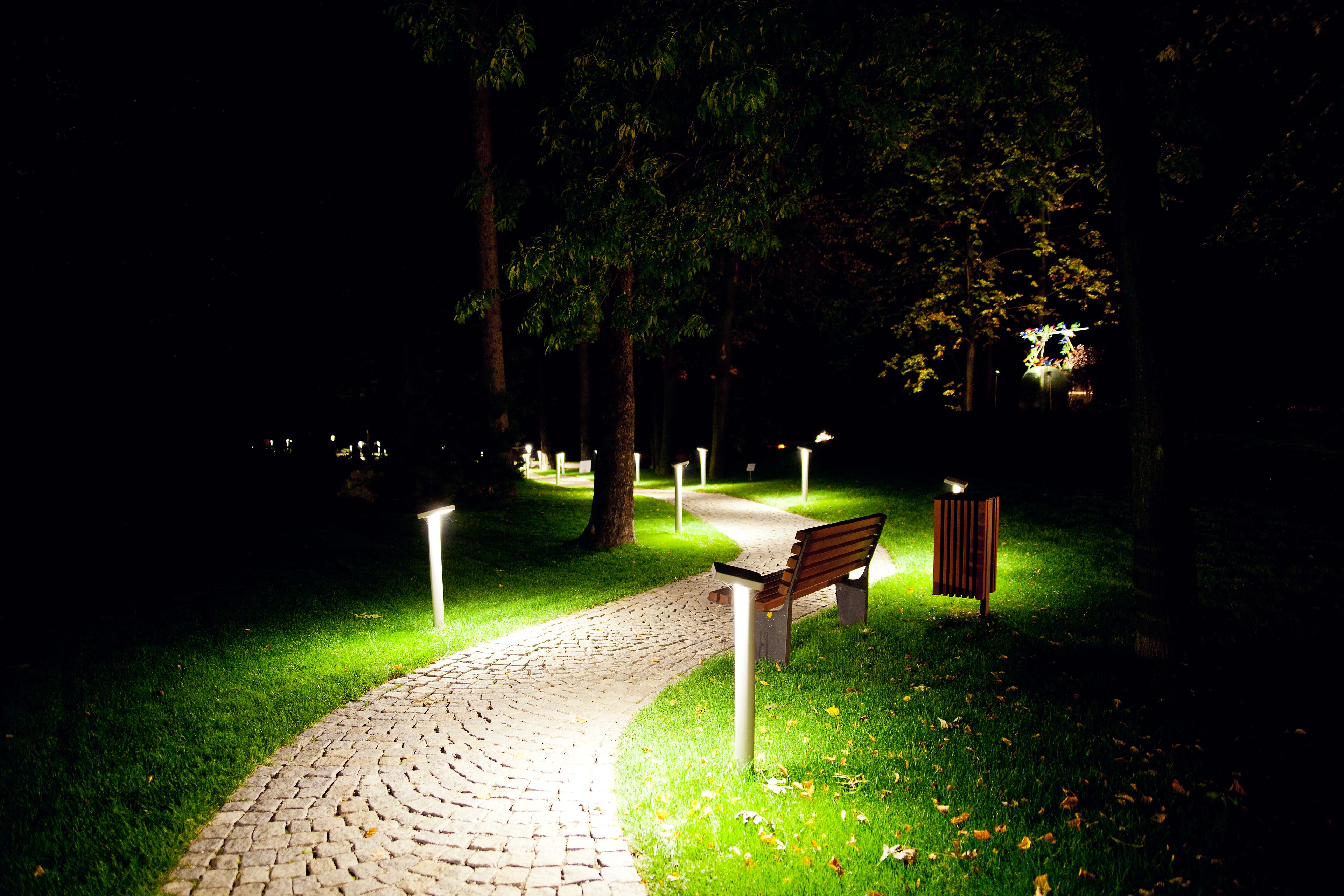 A nighttime park scene with a paved path, a bench, and illuminated posts.