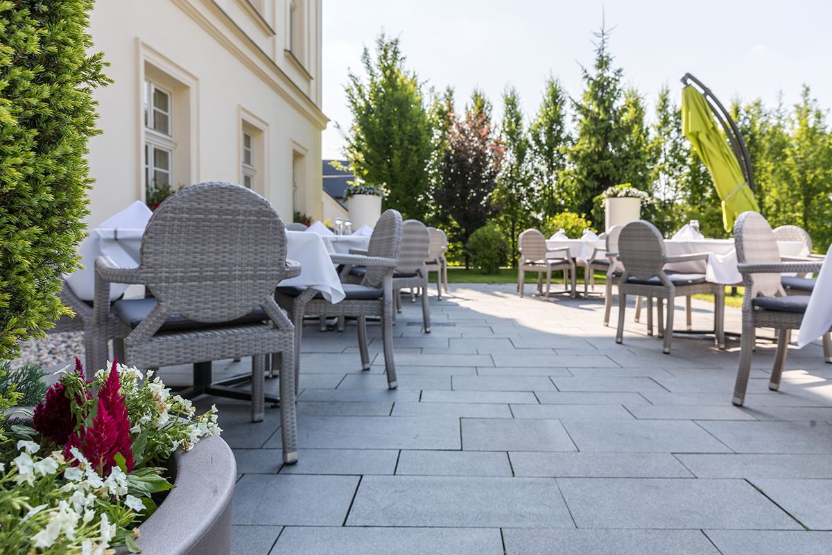 Un patio al aire libre con mobiliario de mimbre y suelo de piedra, rodeado de follaje y un edificio.