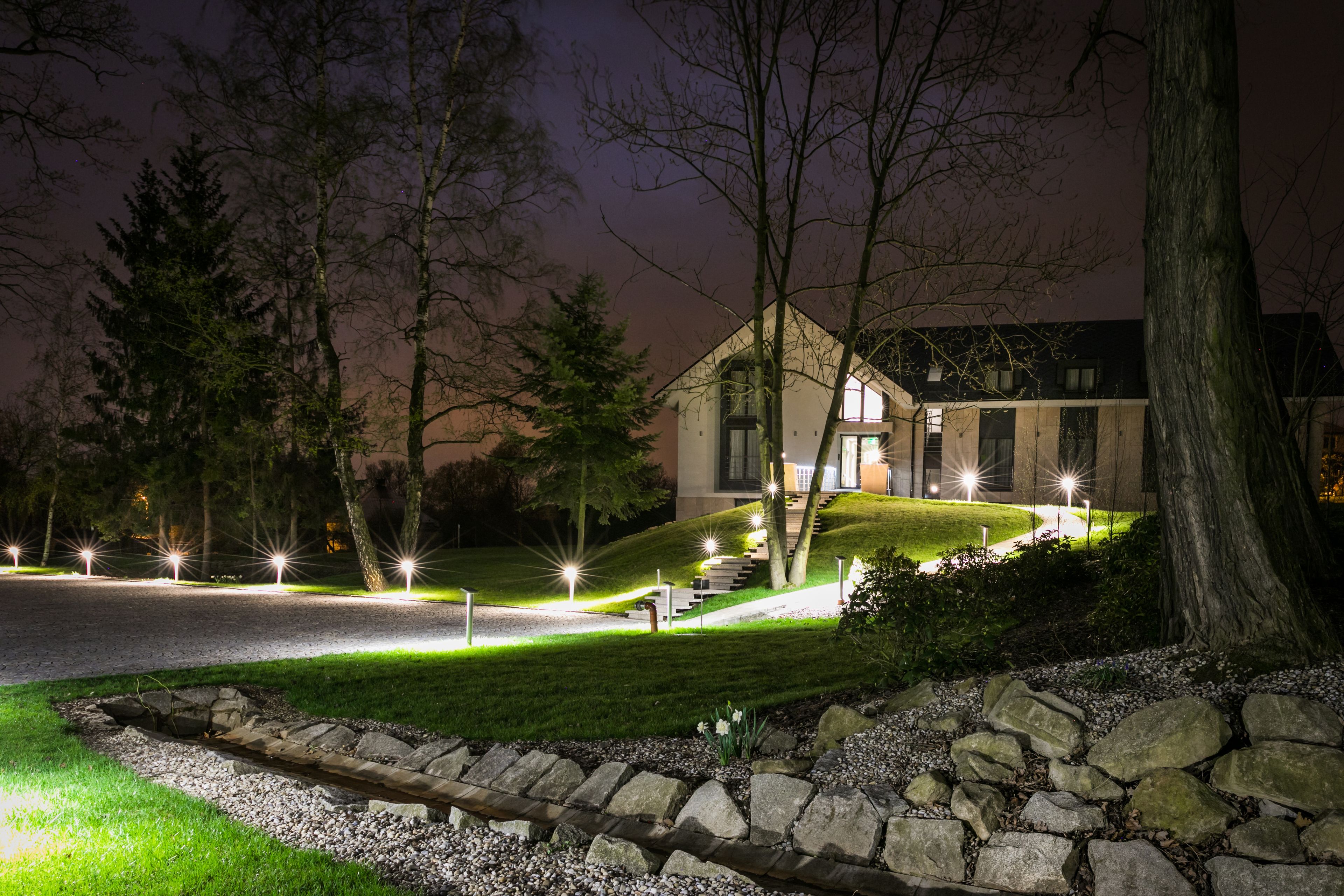 Una casa moderna con un muro de contención de piedra, un camino de entrada bien iluminado y un césped.