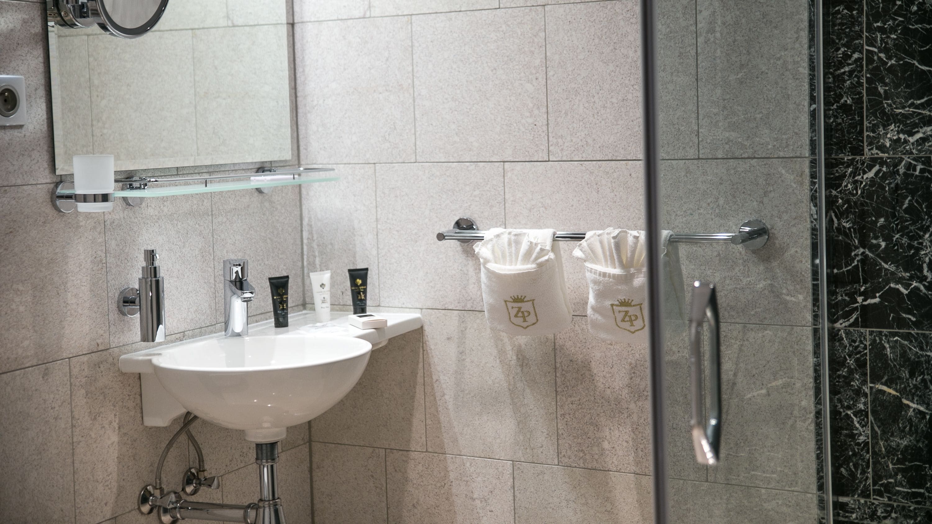 A modern bathroom with a white sink, multiple toiletries, a glass shower enclosure, and a marble backsplash.