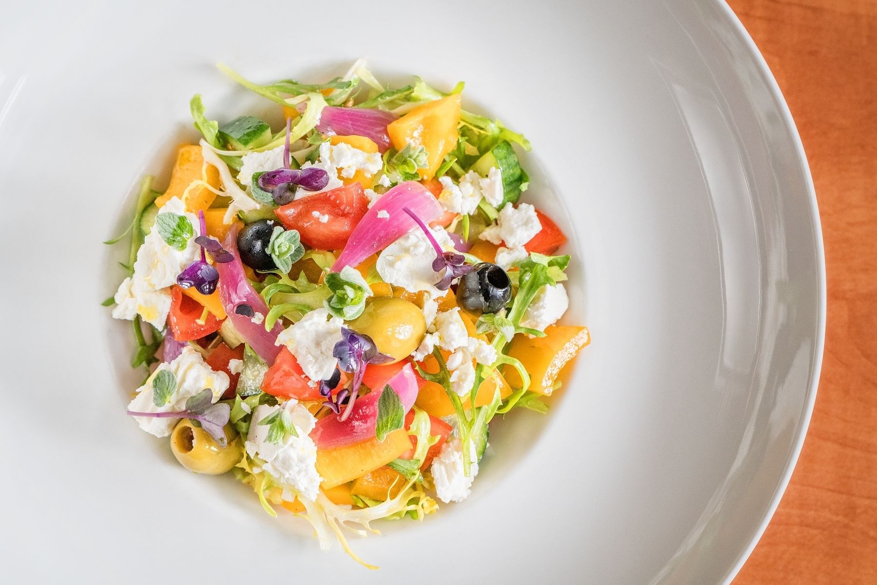 Salada colorida com diversos vegetais e queijo feta em um prato branco.