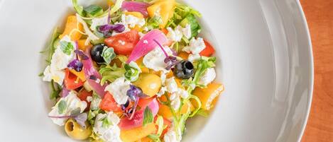 Salada colorida com diversos vegetais e queijo feta em um prato branco.