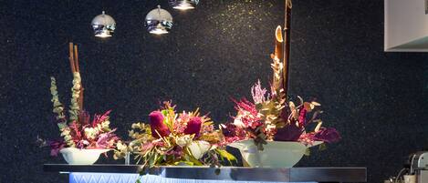 A bar area with a blue bar counter, three white bar stools, and a decorative floral arrangement.
