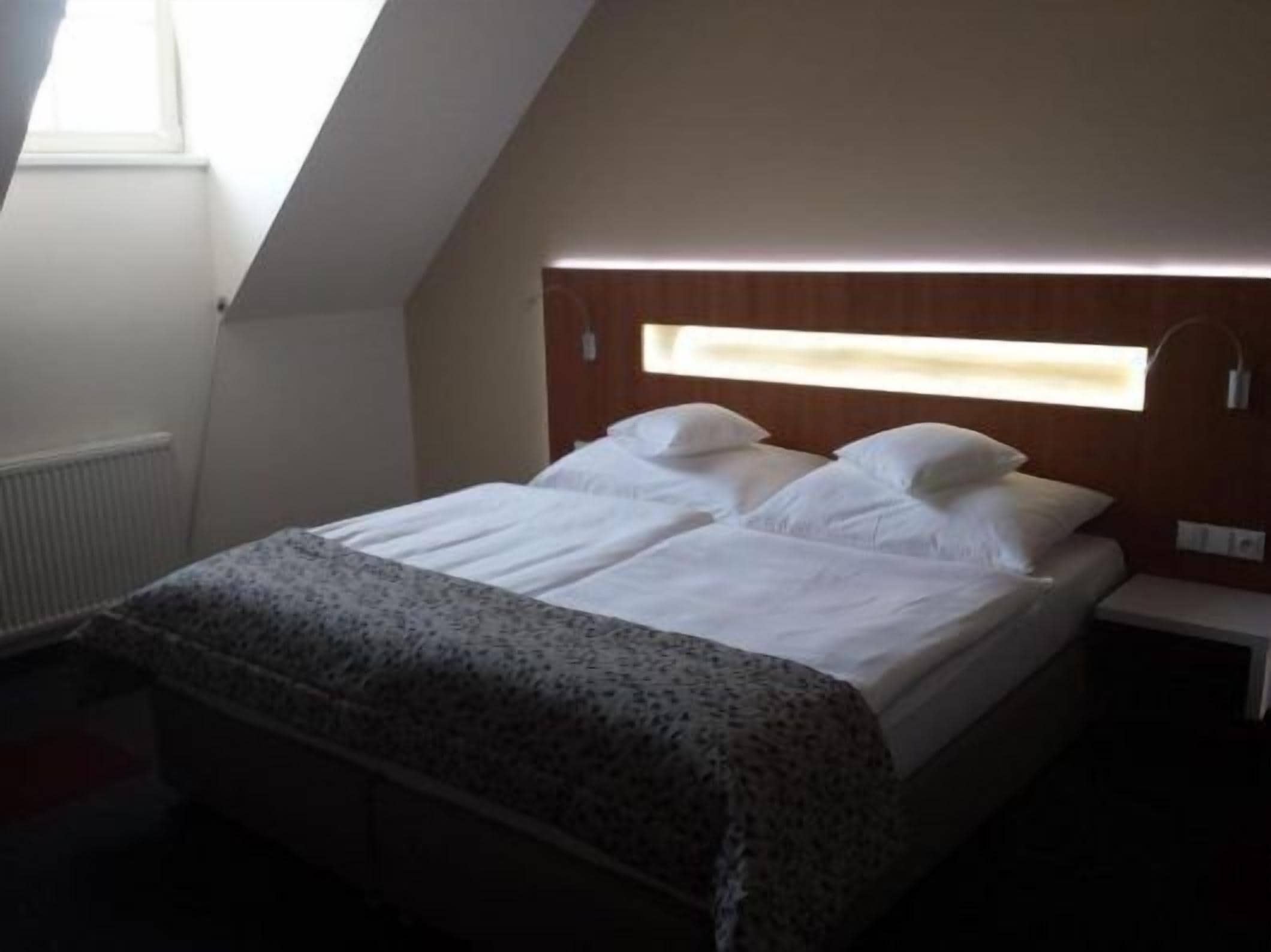 A bedroom with a bed, a bedside table, a window, and a radiator.