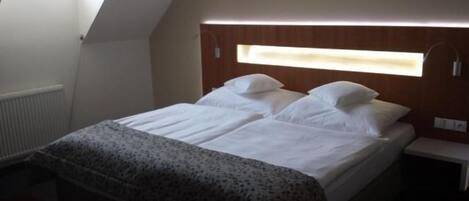 Un dormitorio con cama, mesita de noche, ventana y radiador.