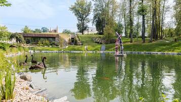 A pond with swans and a statue, surrounded by greenery and a stone bridge.