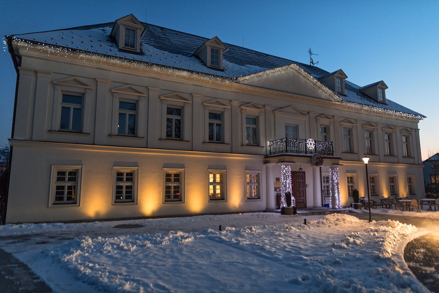 A large, historic building with multiple windows and a snow-covered roof, illuminated by warm lights.