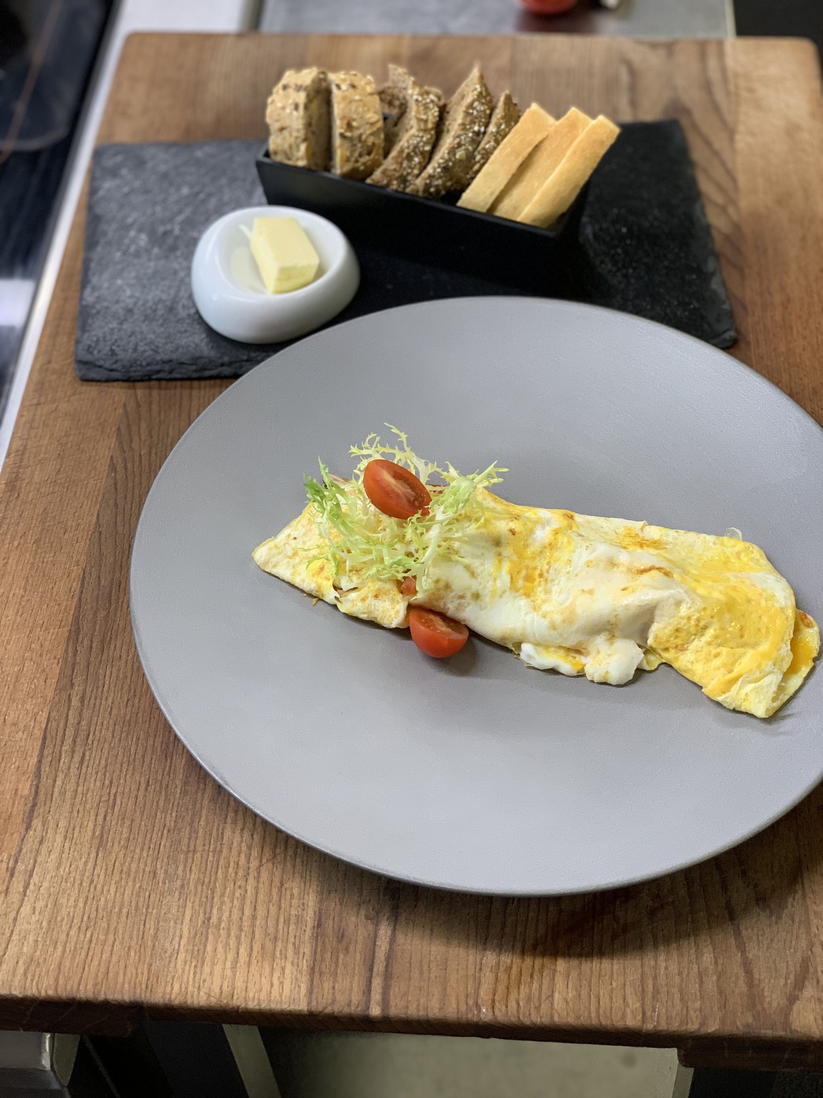 Un plato de comida con una tortilla, un recipiente pequeño de mantequilla y pan en una mesa de madera.