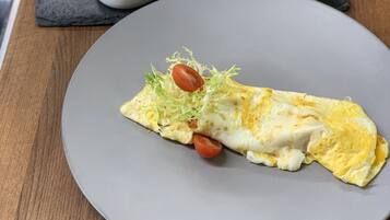 Un plato de comida con una tortilla, un recipiente pequeño de mantequilla y pan en una mesa de madera.