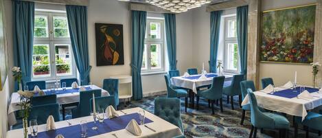 A dining area with tables set for service, blue chairs, and a patterned carpet.