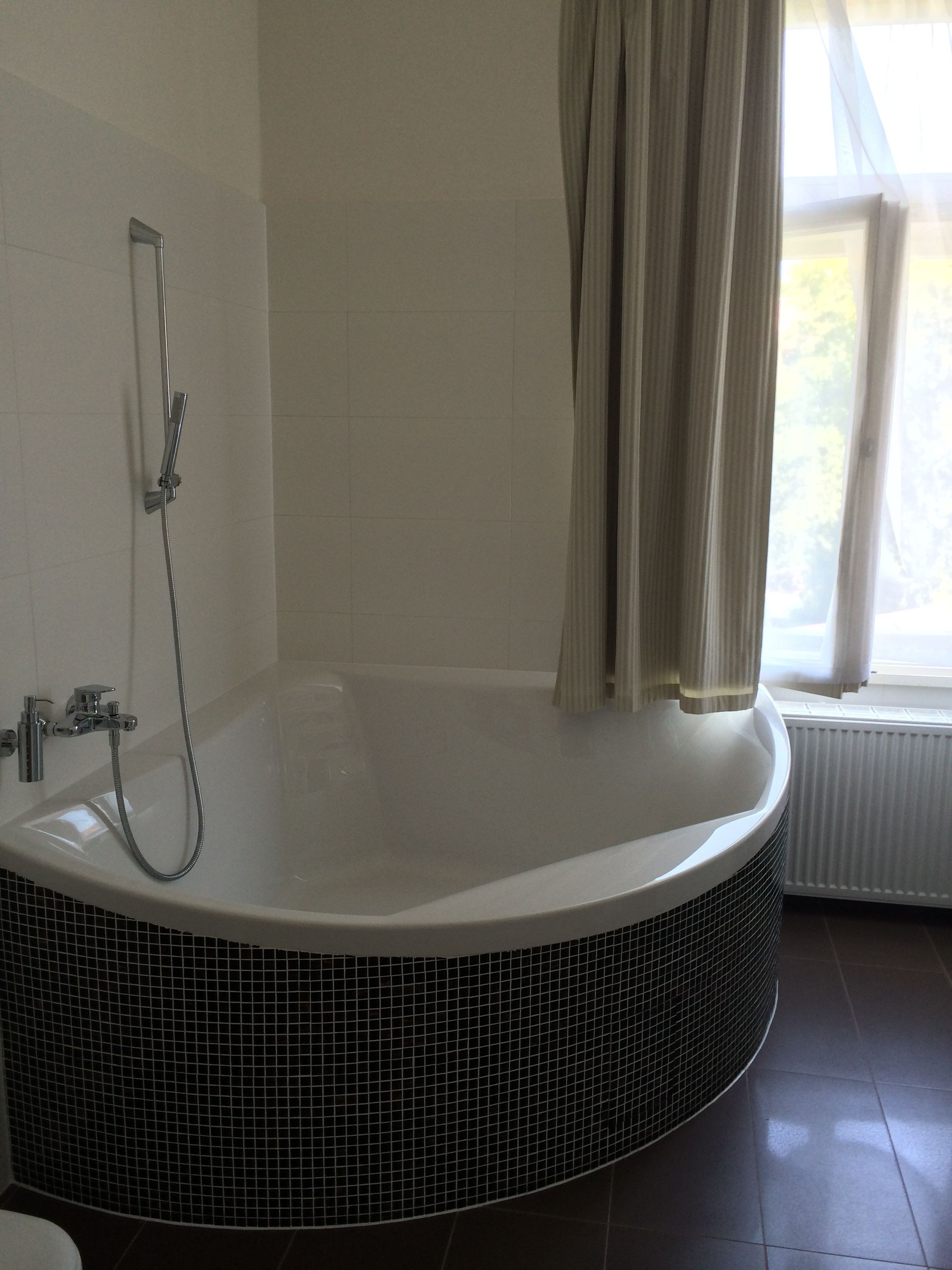 Un baño con una bañera grande y redonda, un cabezal de ducha y una ventana con cortinas.