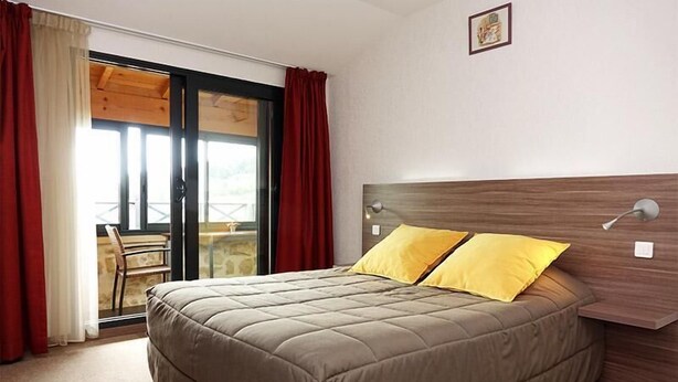 Een slaapkamer met een bed, een houten hoofdbord, een raam met rode gordijnen en uitzicht op een balkon.