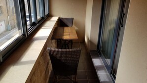 Een smal balkon met een houten tafel en twee rieten stoelen.