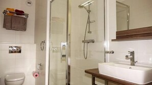 Een badkamer met een douchecabine van glas, een wit wastafelmeubel en een toilet.