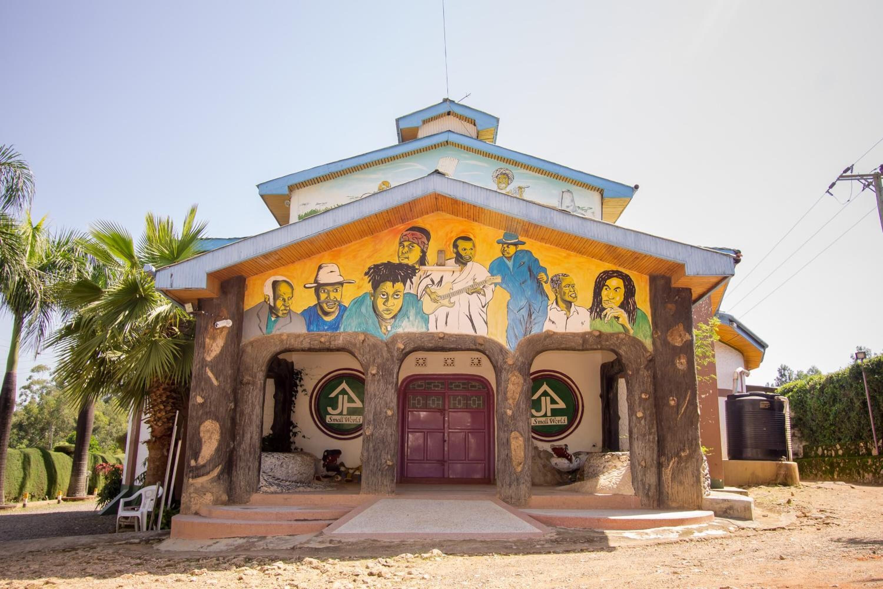 A building with a colorful mural depicting various figures, a purple door, and two green arrows with text.