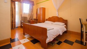 A bedroom with a wooden bed, a wardrobe, a desk, and a chair. - Jamindas Paradise Motel (Kakamega)