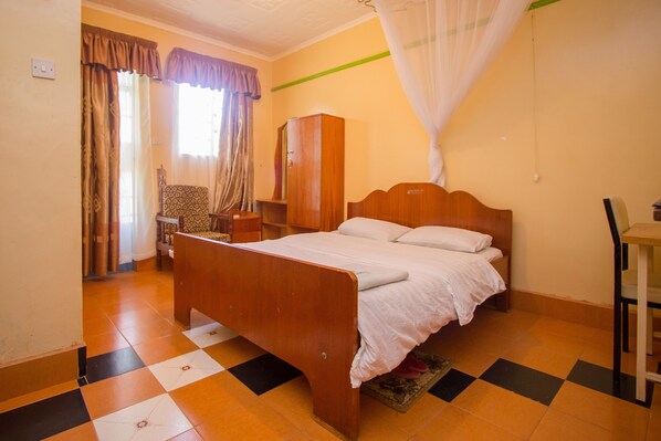 A bedroom with a wooden bed, a wardrobe, a desk, and a chair. - Jamindas Paradise Motel (Kakamega)