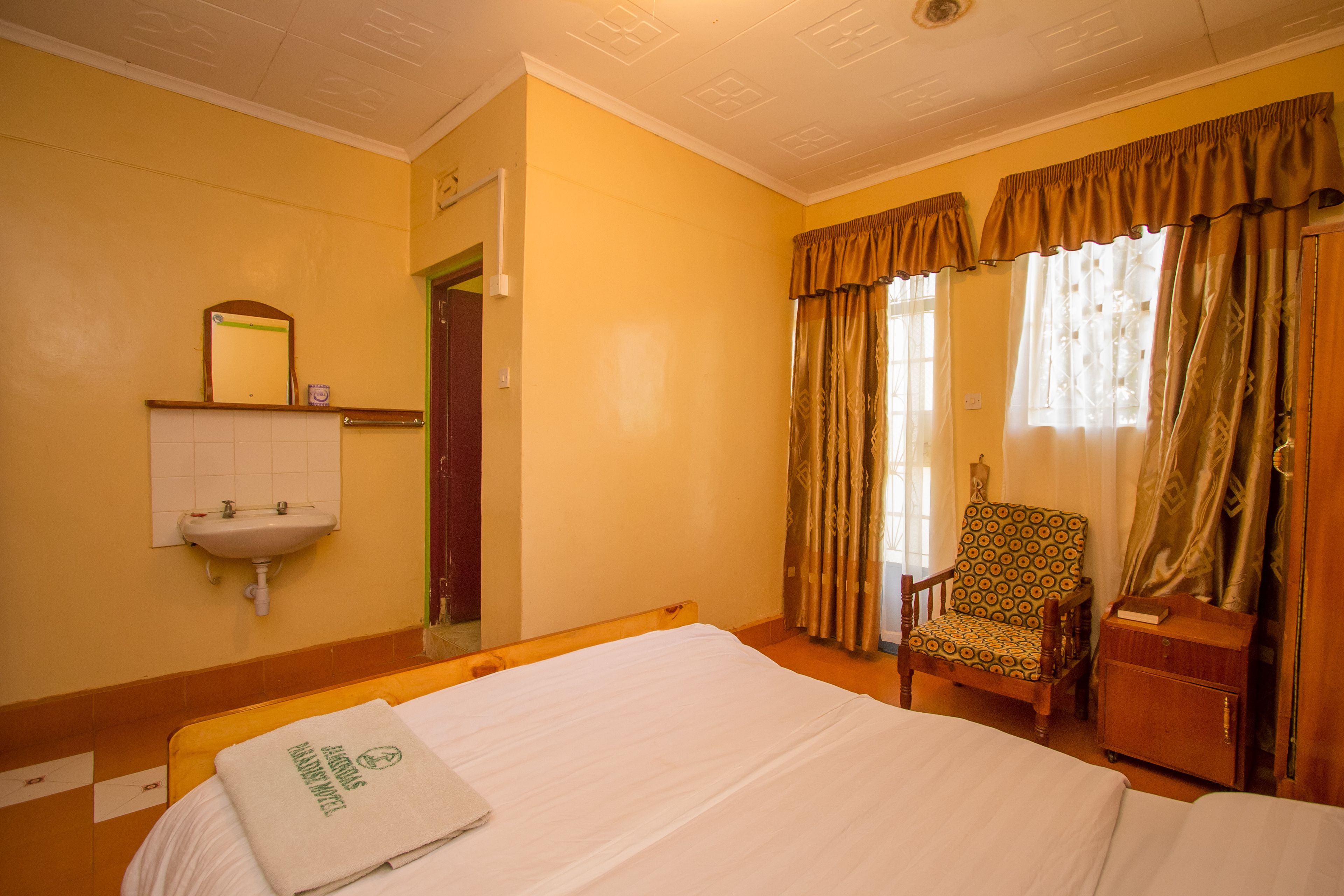 Una habitación de hotel con una cama, una silla, una mesita, un espejo y un lavamanos.