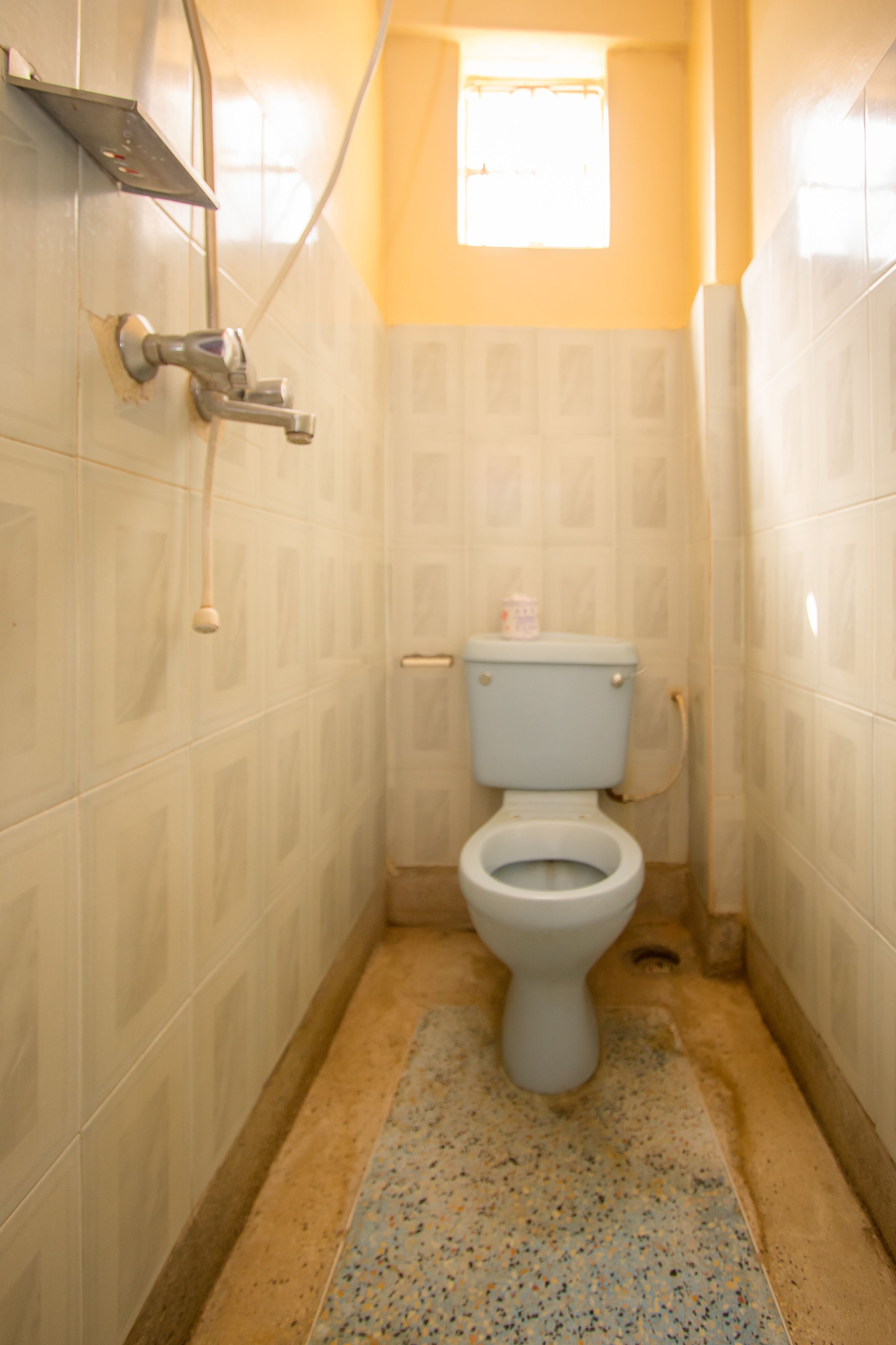A small, narrow bathroom with a toilet, a showerhead, and a window.