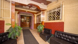 A lobby with a central black carpet, two black leather sofas, potted plants, a wooden ceiling, and a red brick wall. - Jamindas Paradise Motel (Kakamega)