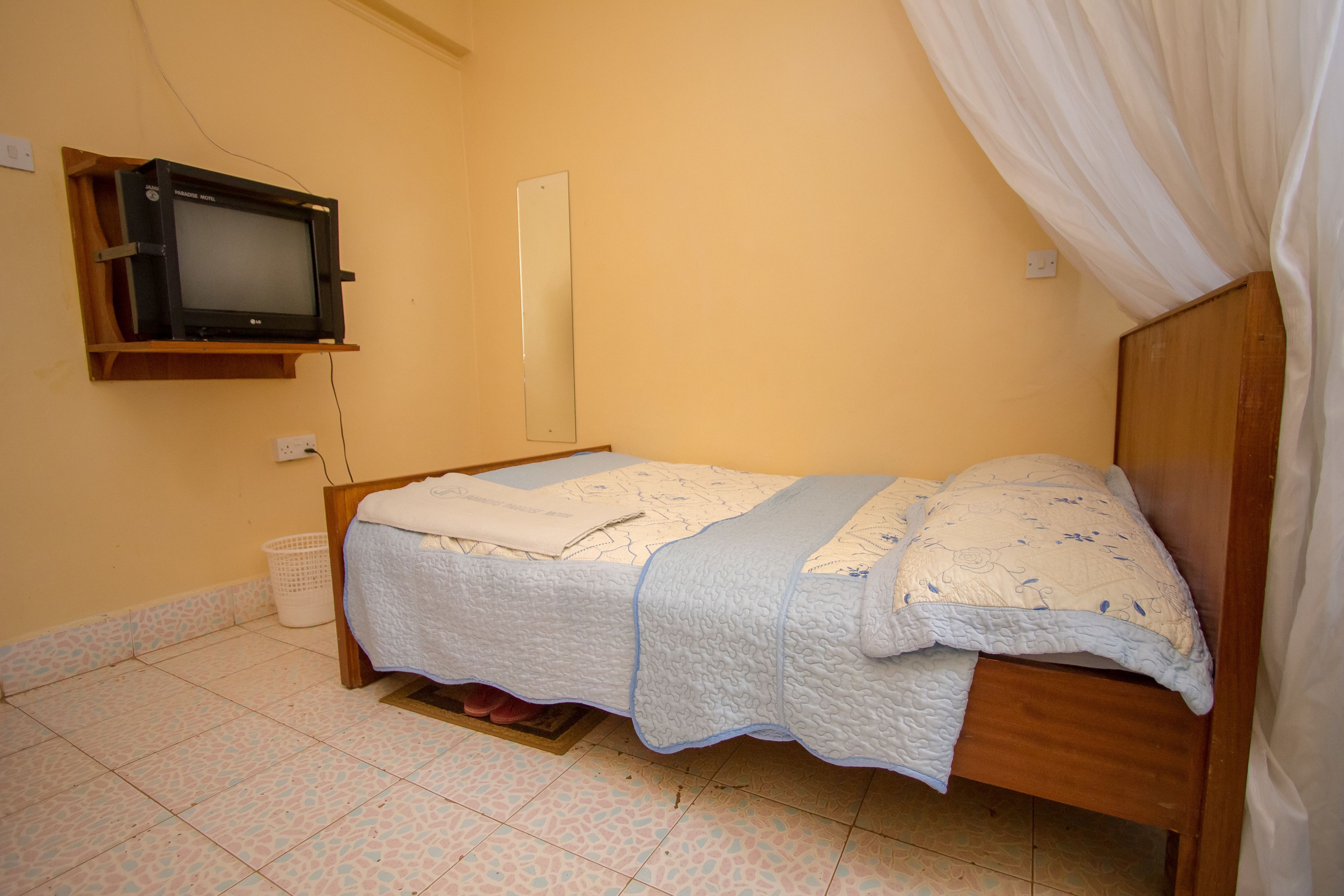 Un dormitorio con una cama, un televisor en la pared, un espejo y una cortina.