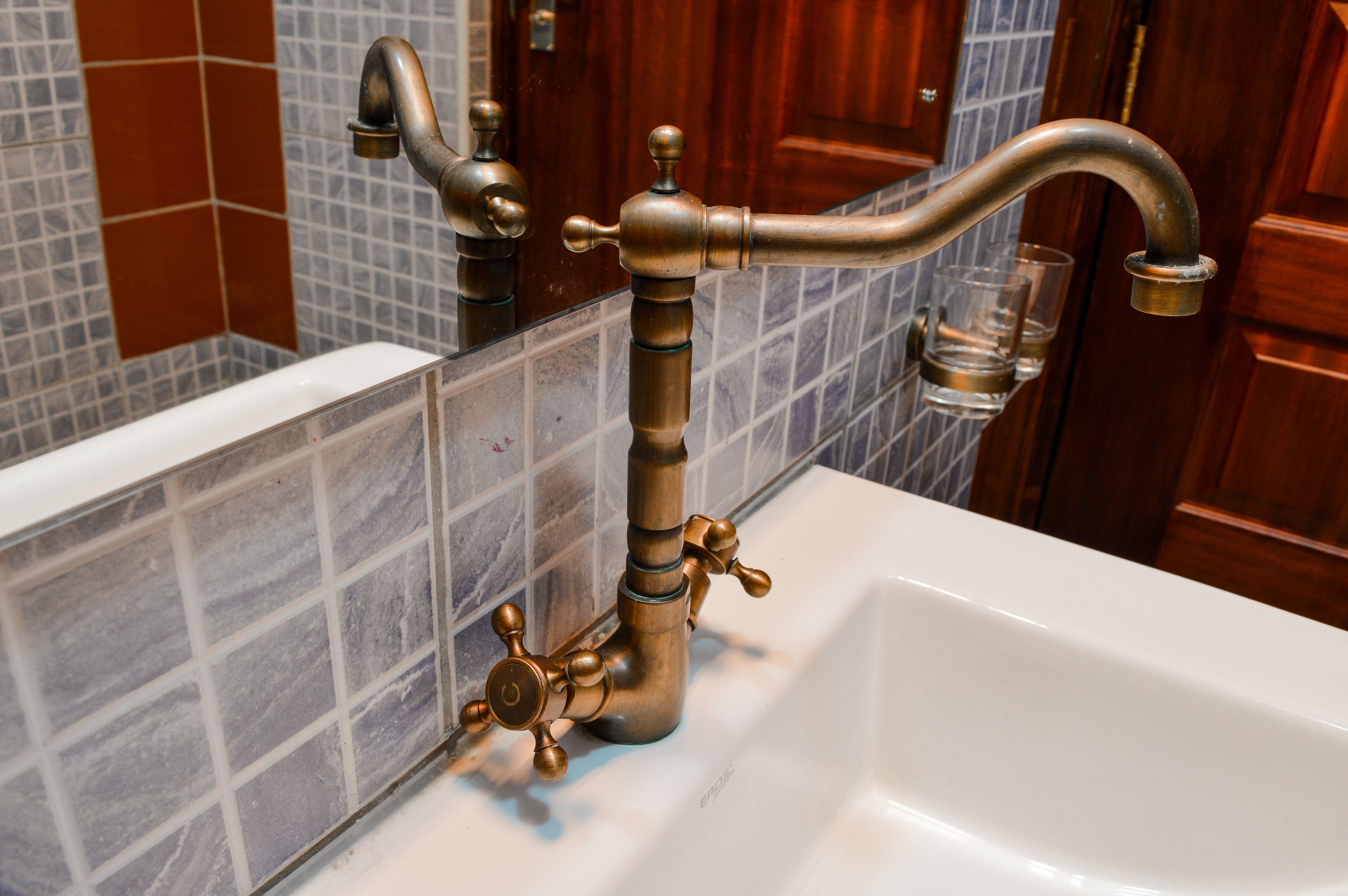 A bathroom with a white bathtub, a brass faucet, and a tiled wall.