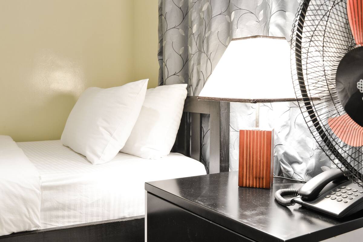 A hotel room with a bed, a bedside table with a lamp, a telephone, and a decorative item.