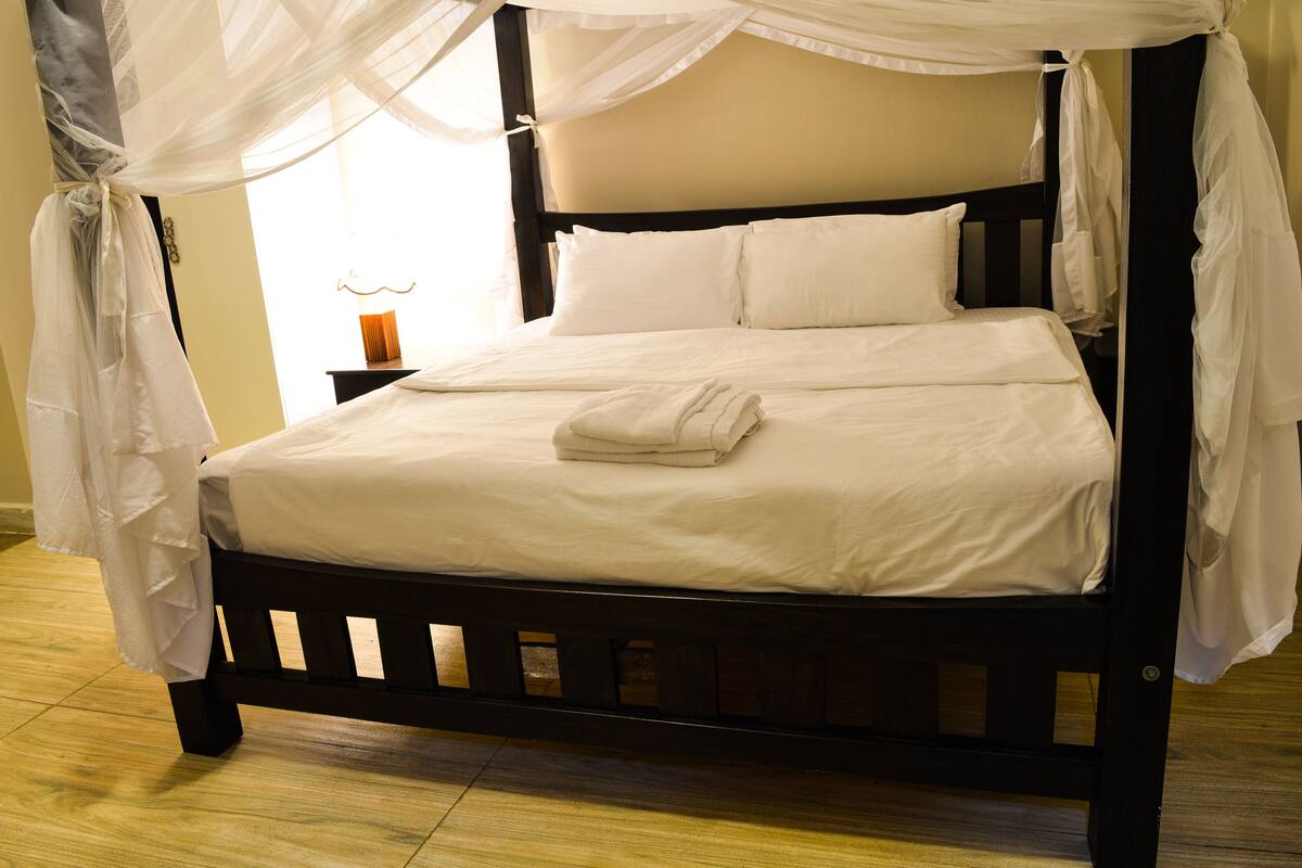 A bed with white linens, a canopy, and a bedside table with a lamp.