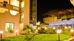 Un hotel con un espacio exterior luminoso que cuenta con un jardín con césped, palmeras y un borde de piedra.