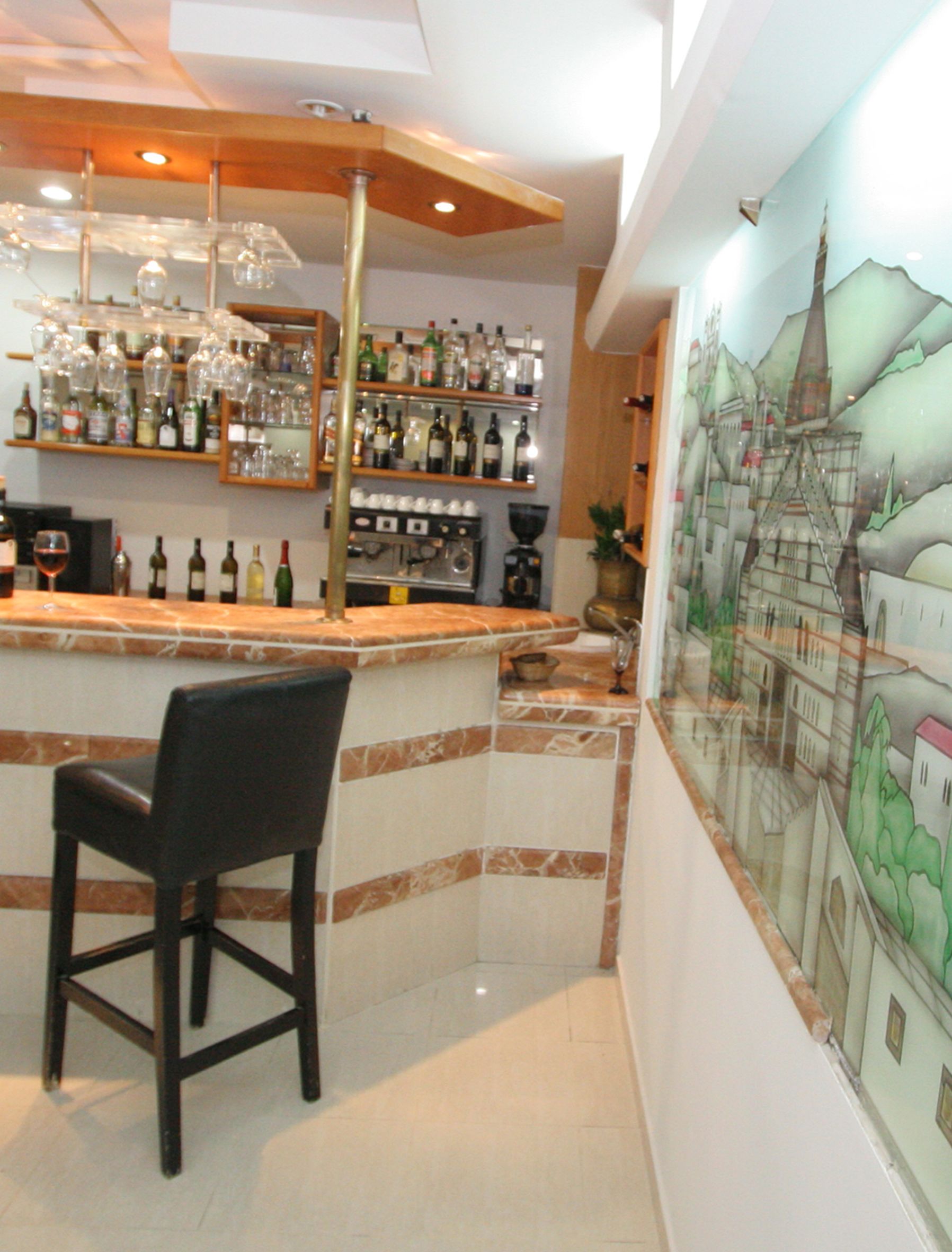 A bar area with a counter, shelves of bottles, glasses, and a mural on the wall.