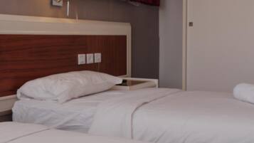 Habitación de hotel con dos camas, cabecero de madera, mesita de noche, lámpara y cortinas rojas.