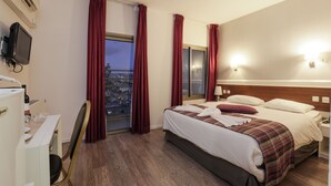 Une chambre d’hôtel avec un lit, un bureau avec un ordinateur, une chaise et une fenêtre avec des rideaux.
