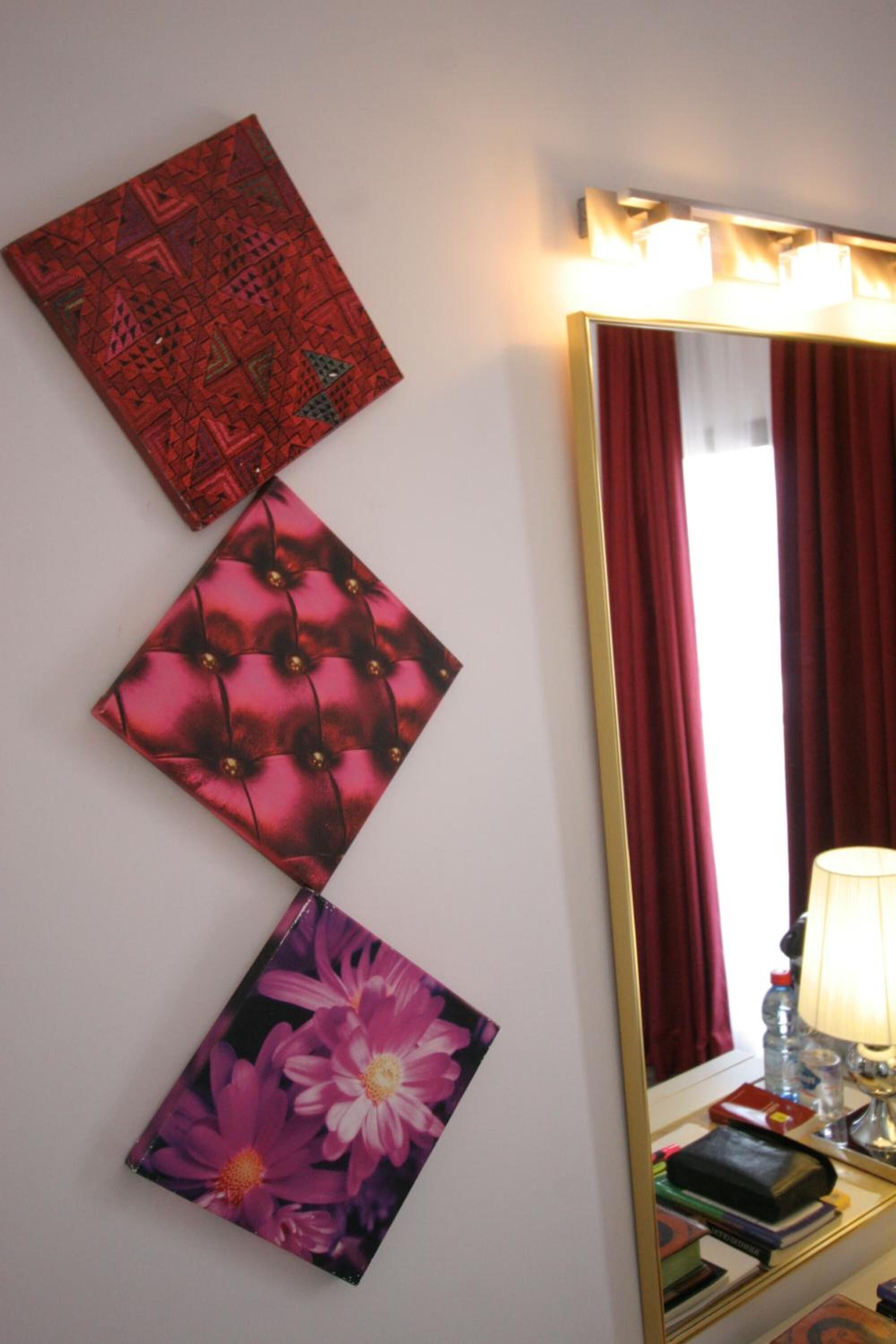A mirror with a gold frame, a red curtain, and a bedside table with a lamp and books.