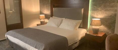 A modern hotel room with a large bed, marble walls, and two bedside lamps.